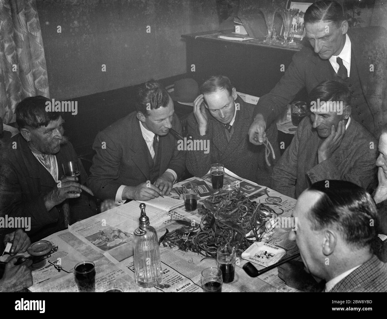 Paying in night at the Rat and Sparrow Club in Eynsford , Kent . Charlie Meadows drinks his beer on the left side of the picture next to Mr F Foreman the secretary . Foreman is tallying up the rat 's tails on the table . Member are being paid according to the number of rat 's tails in their catch . 1939 Stock Photo