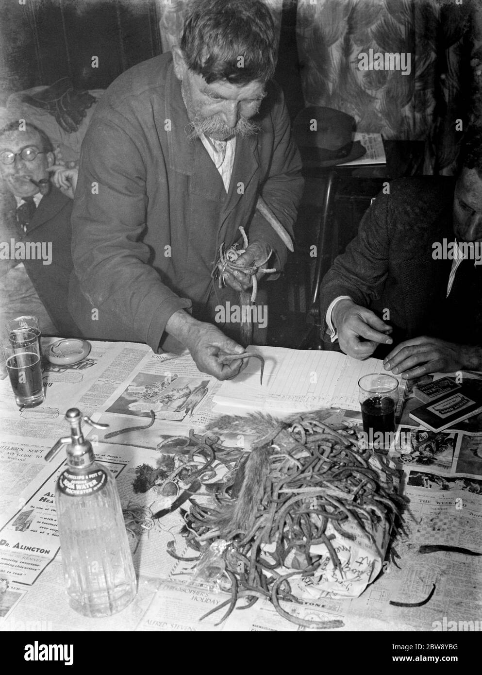 Paying in night at the Rat and Sparrow Club in Eynsford , Kent . Charlie Meadows paying in his catch of rat 's tails . Members get paid according to the number of rat 's tails in their catch . 1939 Stock Photo