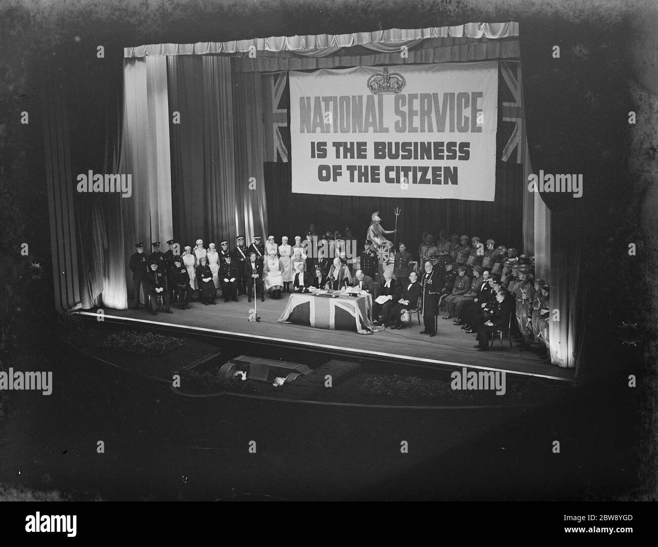 ' National Service is the business of the citizen ' . A tableau depicting voluntary organizations was staged at the Regal Cinema in Bexleyheath , Kent , in order to encourage people to train up in case of an emergency . The Police , Fire Service , Territorial Army , Air Raid Precaution , Red Cross , St John Ambulance , Boy Scouts and the Decontamination Service all took part . 15 April 1939 Stock Photo