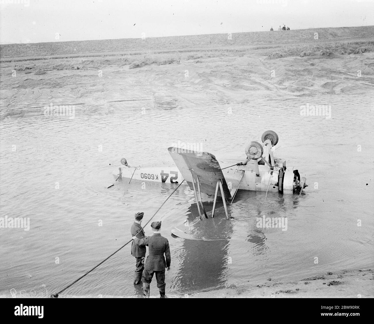 Royal Air Force personnel attempt to recover the Avro 621 Tutor K6090 plane at low tide with a rope round the landing strut of the aircraft in the hope of pulling it to drier land . The plane is lying upside down in Dartford Creek following a crash . 31 January 1939 Stock Photo