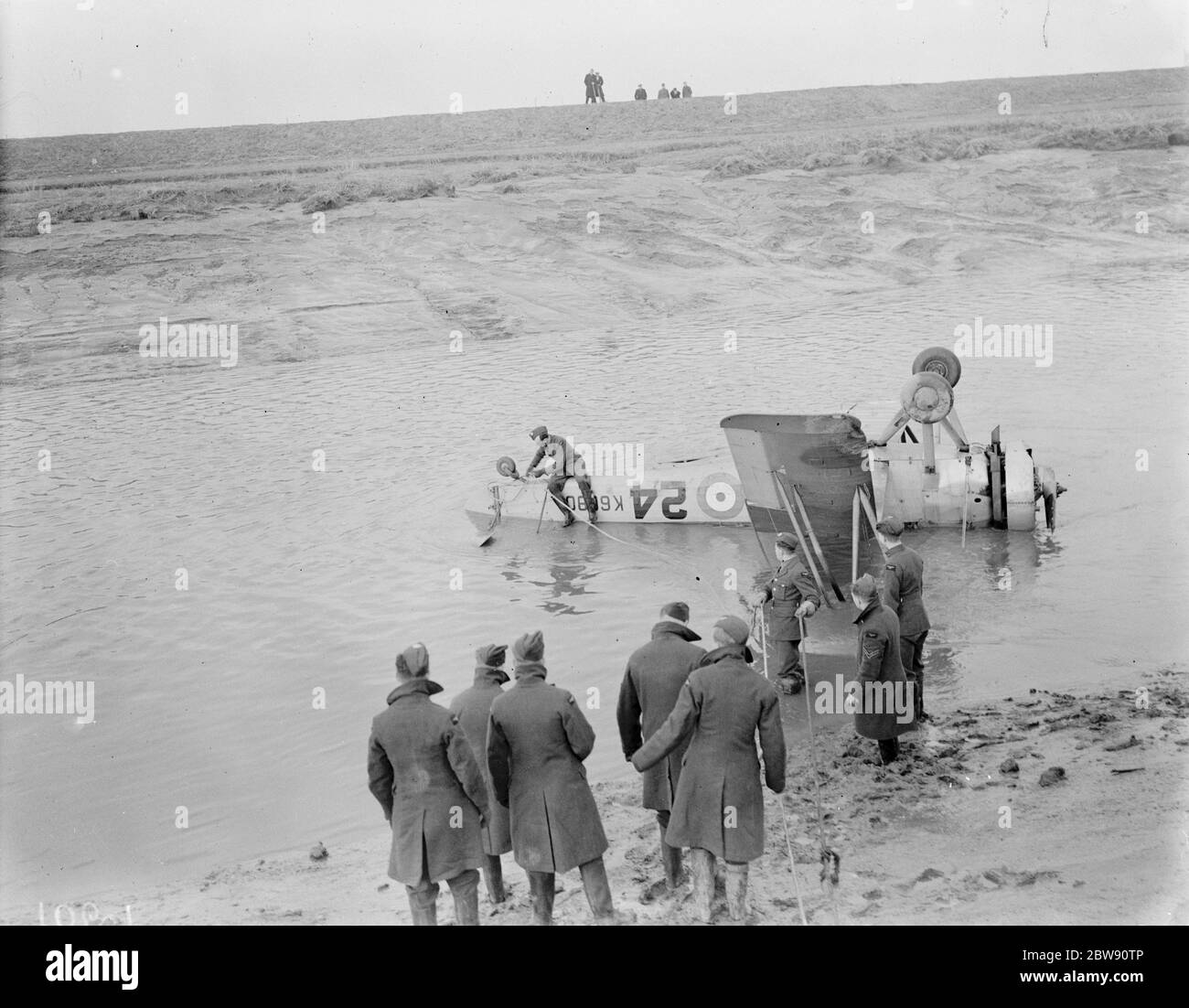 Royal Air Force personnel attempt to recover the Avro 621 Tutor K6090 plane at low tide with a rope round the landing strut of the aircraft in the hope of pulling it to drier land . The plane is lying upside down in Dartford Creek following a crash . 31 January 1939 Stock Photo