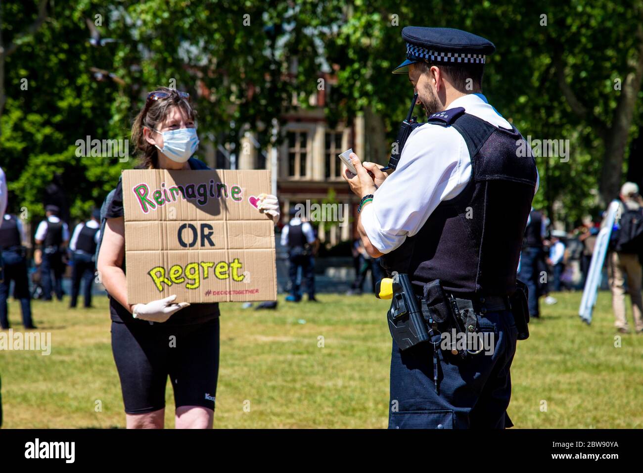 30 May 2020 London, UK - Extinction Rebellion stage silent socially-distanced climate change protest in Westminster, protesters being fined and taken away by police for breaching coronavirus regulations, police office writing a fine ticket to a woman holding a sign 'Reimagine or Regret' Stock Photo