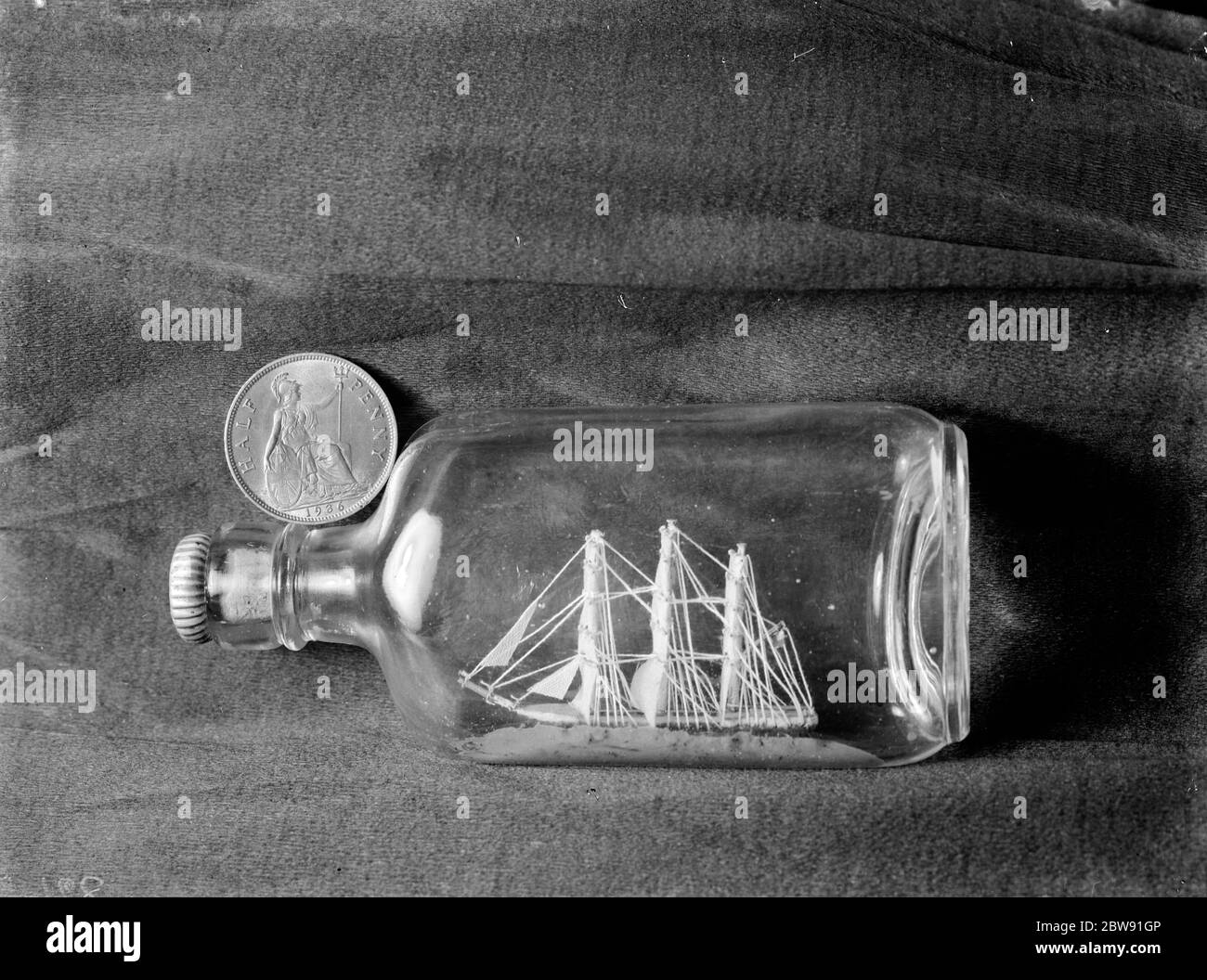 A small model ship in bottle compared to the size of a penny . 1938 Stock Photo