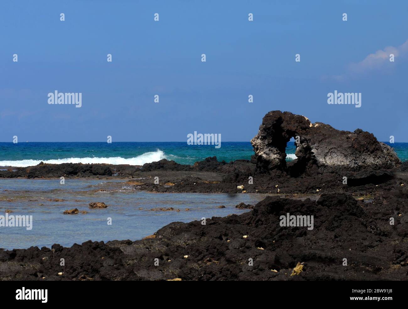 Lava arch on the Kohala Coast on the Big Island of Hawaii is surrounded by vivid aqua water.  Background image with space for personalization. Stock Photo