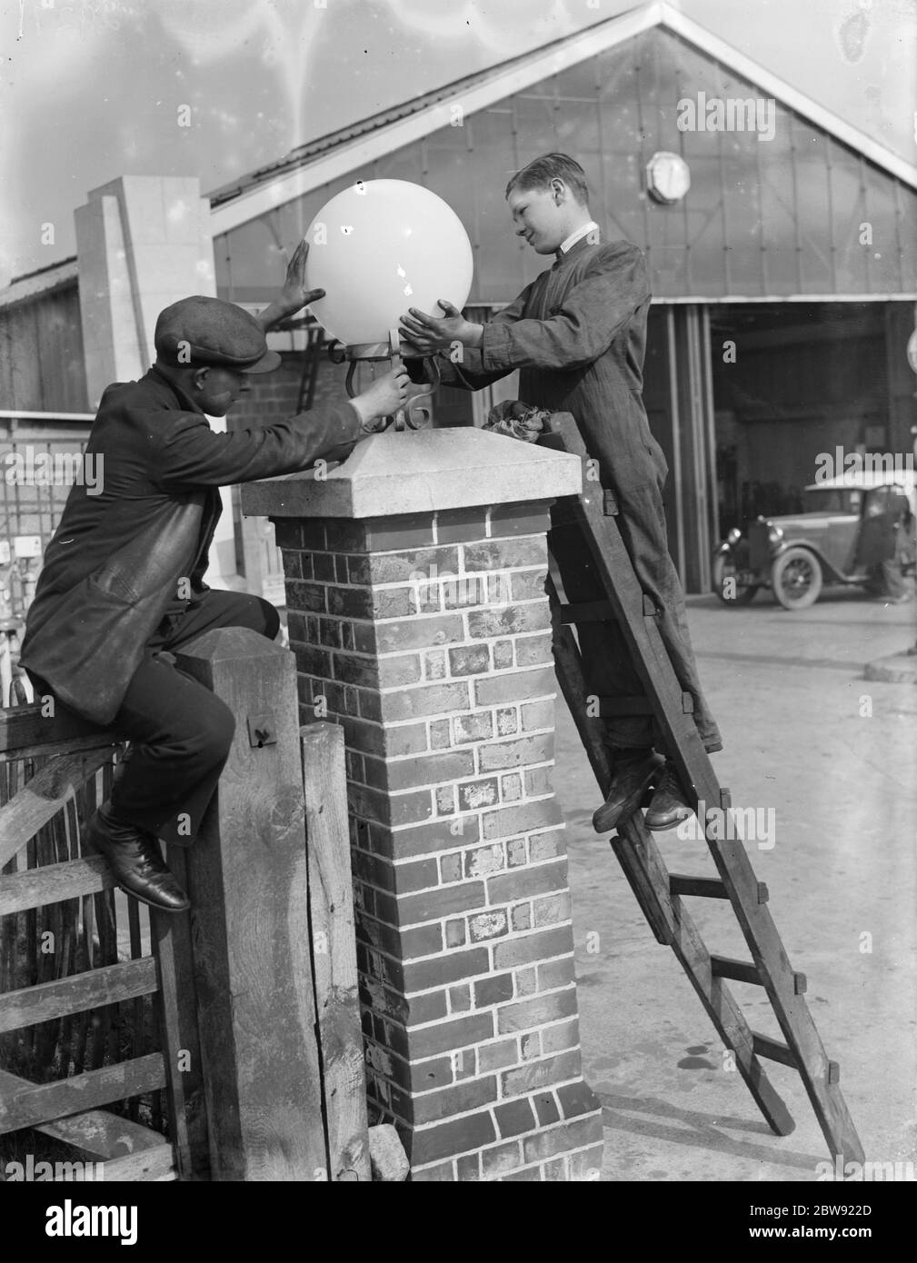 Workmen repairing a light on a garage forecourt . 1936 . Stock Photo