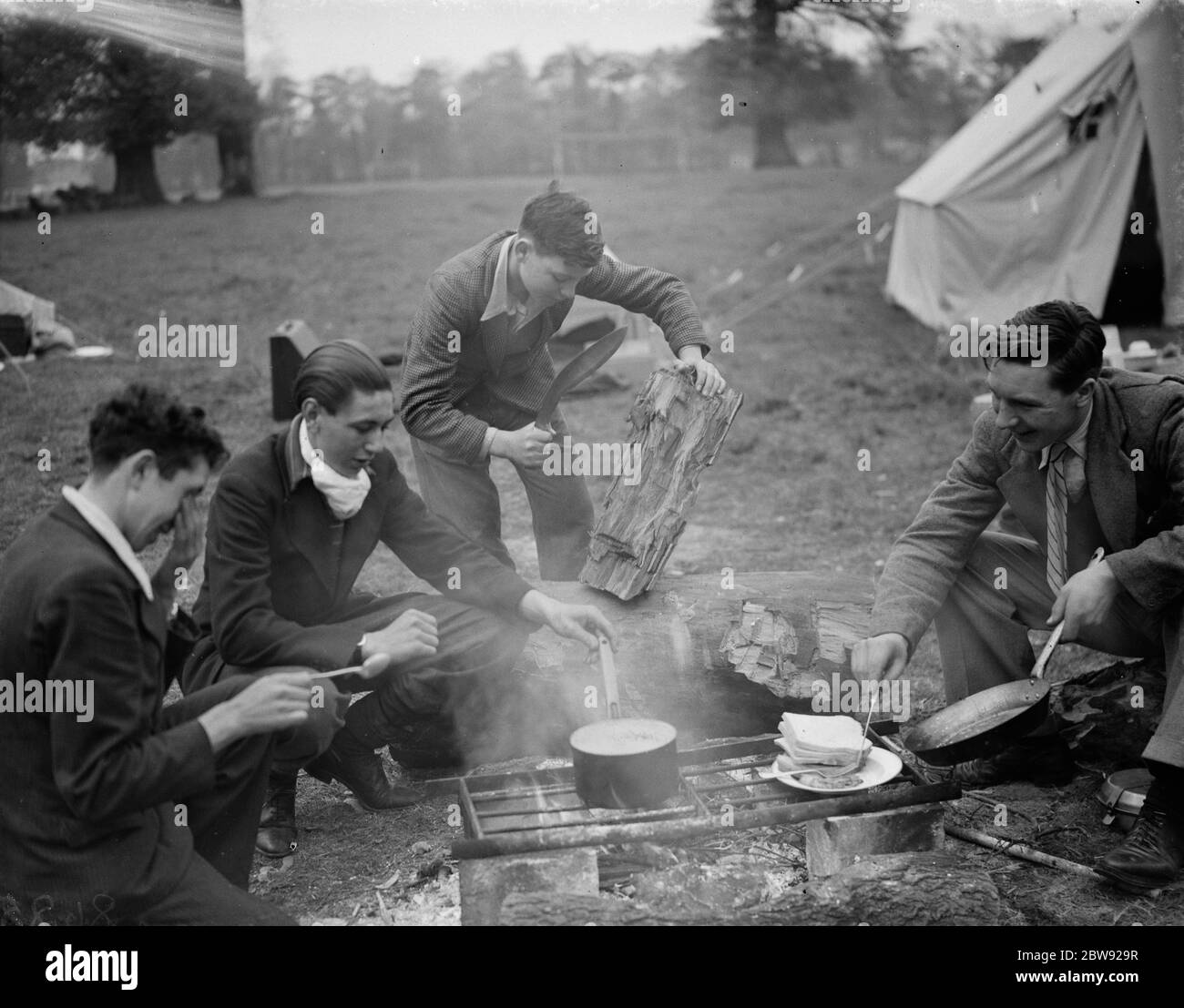 Chopping wood ( with a kukri , Nepalese knife ) and cooking around the camp fire at the Evening Institute camp at Frognal , Sidcup , Kent . 1938 Stock Photo