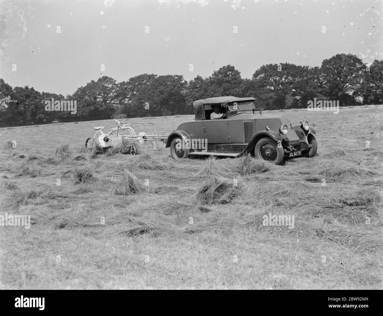 A farmer haymaking in a field using a car to pull the machinery . 1939 Stock Photo