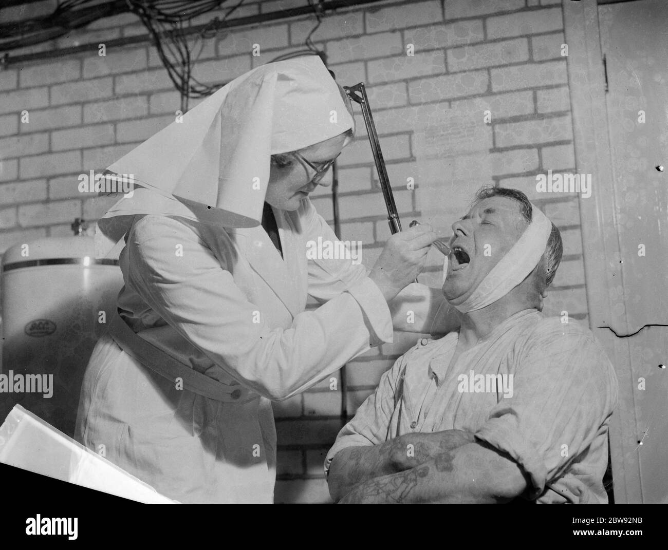 An emergency underground hospital in Erith , London . Nurse examines a  patient ' s  mouth during a training drill . 1939 Stock Photo