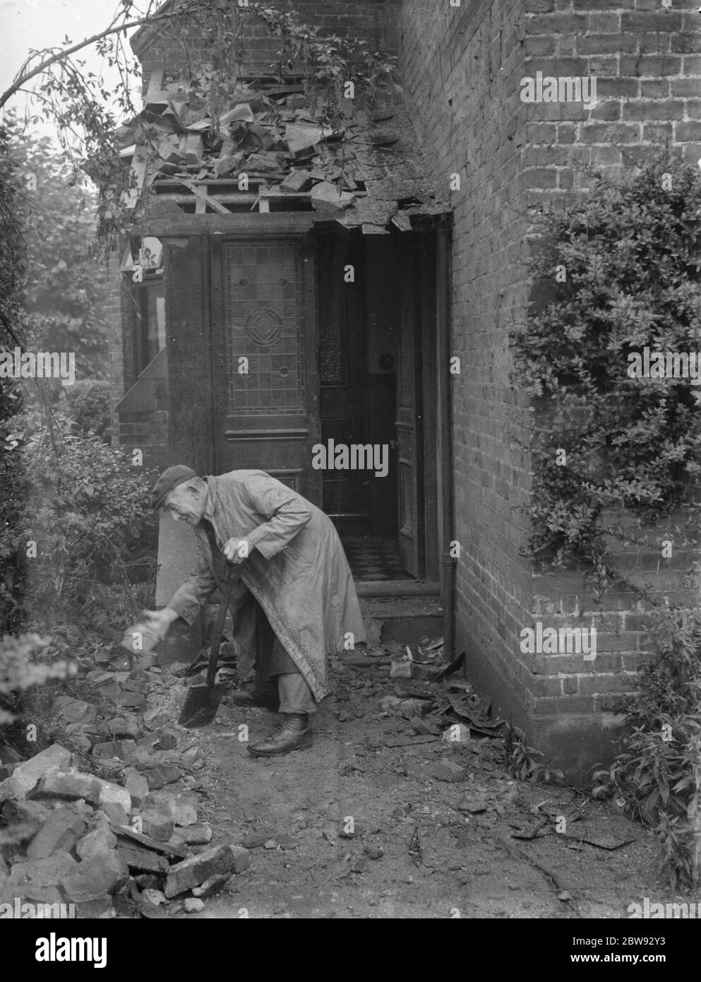 A man is trying to clear the rubble from a house that has been damaged by lightning on Station Road . 1939 Stock Photo