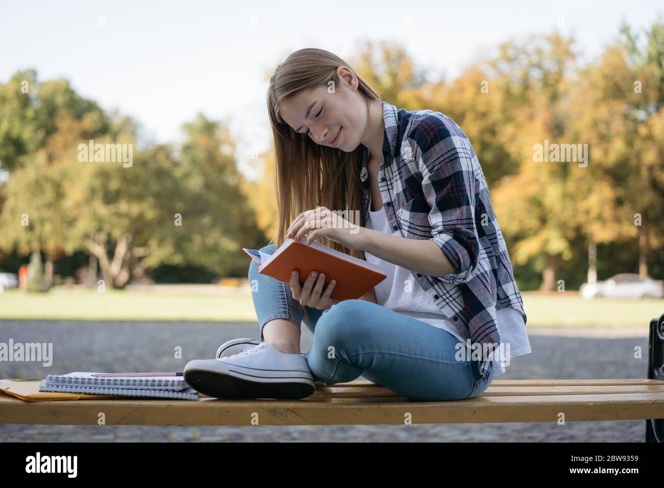 Beautiful woman reading a book sitting on bench. Student studying, learning language, exam preparation, working project in park. Education concept Stock Photo