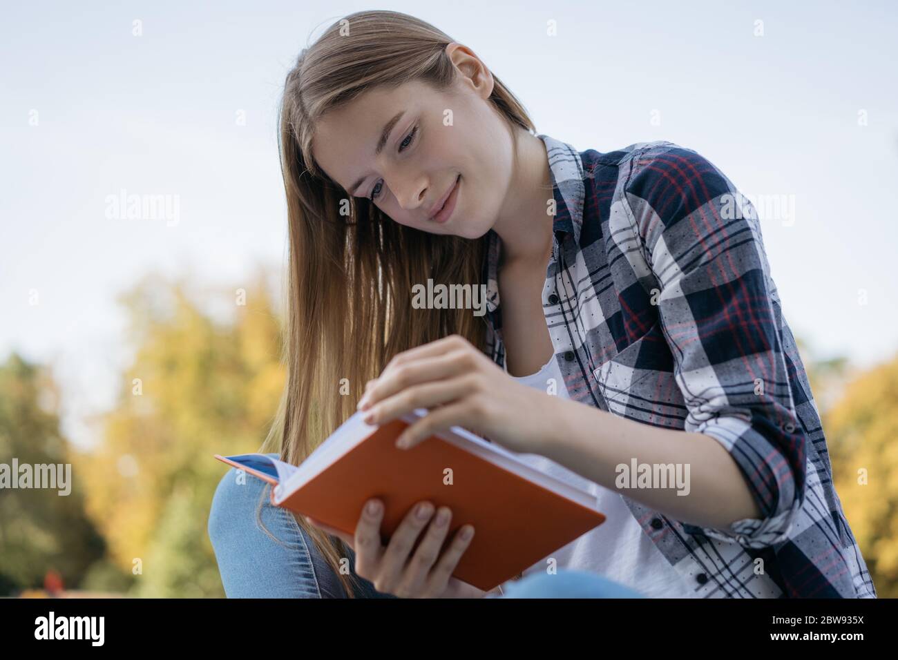 Beautiful woman reading book in park. Close up portrait of smiling student learning language, exam preparation, sitting on bench. Education concept Stock Photo