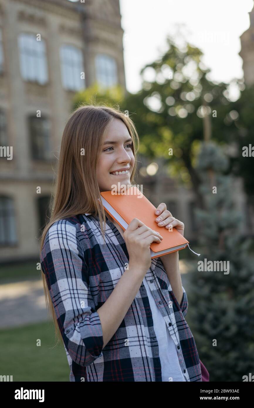 Student with backpack and book walking at home after good exam results. Education concept. Portrait of happy beautiful woman standing in park Stock Photo