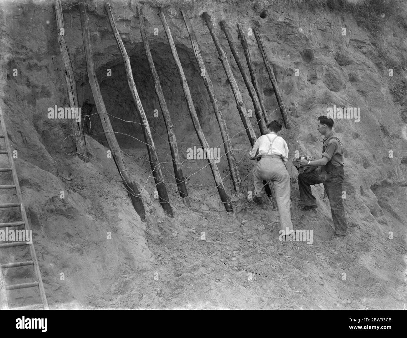 A dangerous hole in a cliff is being fenced off wall . 1939 Stock Photo