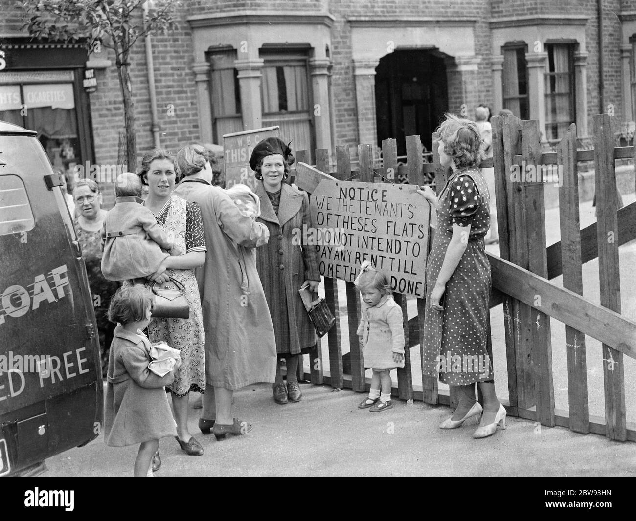 Residents of a street in Plumstead stage a small demonstration in reaction to how the authorities have dealt with the subsidence which has closed their road . They stand at the road barrier with a sign the reads : ' Notice : We the tenants of these flats do not intend to pay and rent till something is done ' . 1939 Stock Photo