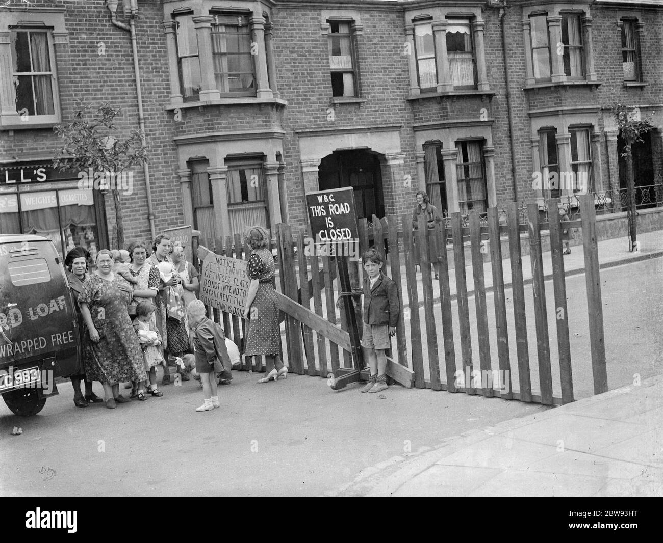 Residents of a street in Plumstead stage a small demonstration in reaction to how the authorities have dealt with the subsidence which has closed their road . They stand at the road barrier with a sign the reads : ' Notice : We the tenants of these flats do not intend to pay and rent till something is done ' . 1939 Stock Photo