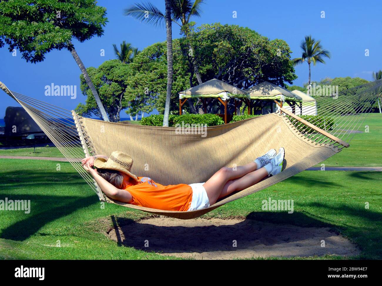 Older woman lays in a hammock slung between two palm trees on a resort ...