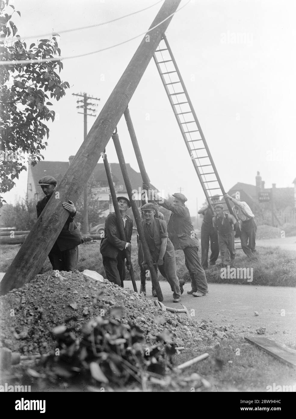 workers use ladders and poles erect an electric pylon next to a road in