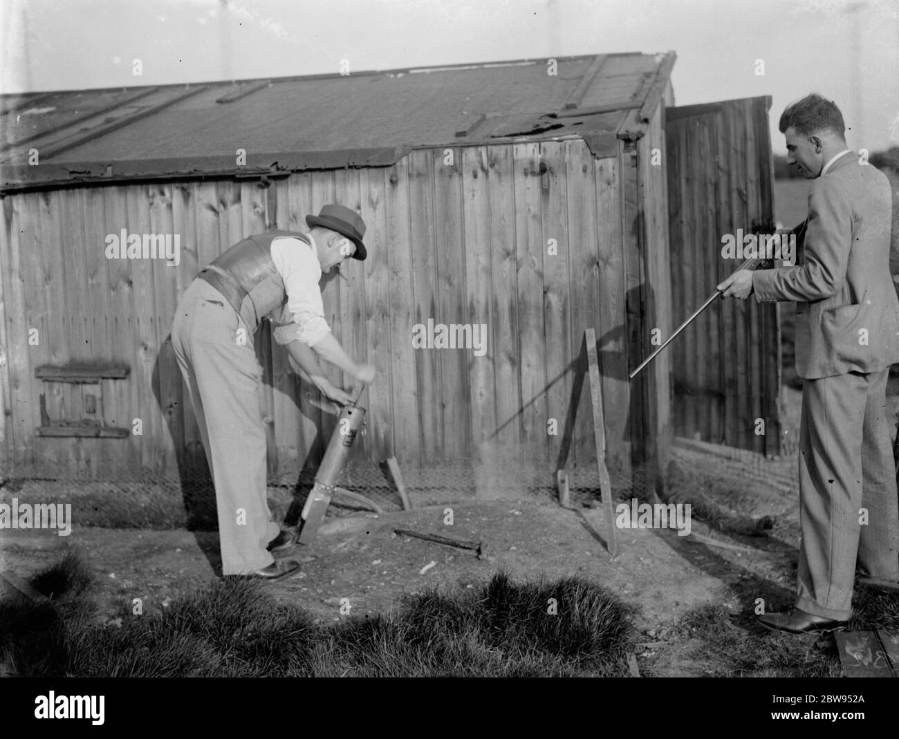 A cyanogas demonstration . Whilst one of the men pumps the gas into the rat borrow another stands by with a rifle , ready to shoot any rats that run out . 1936 Stock Photo