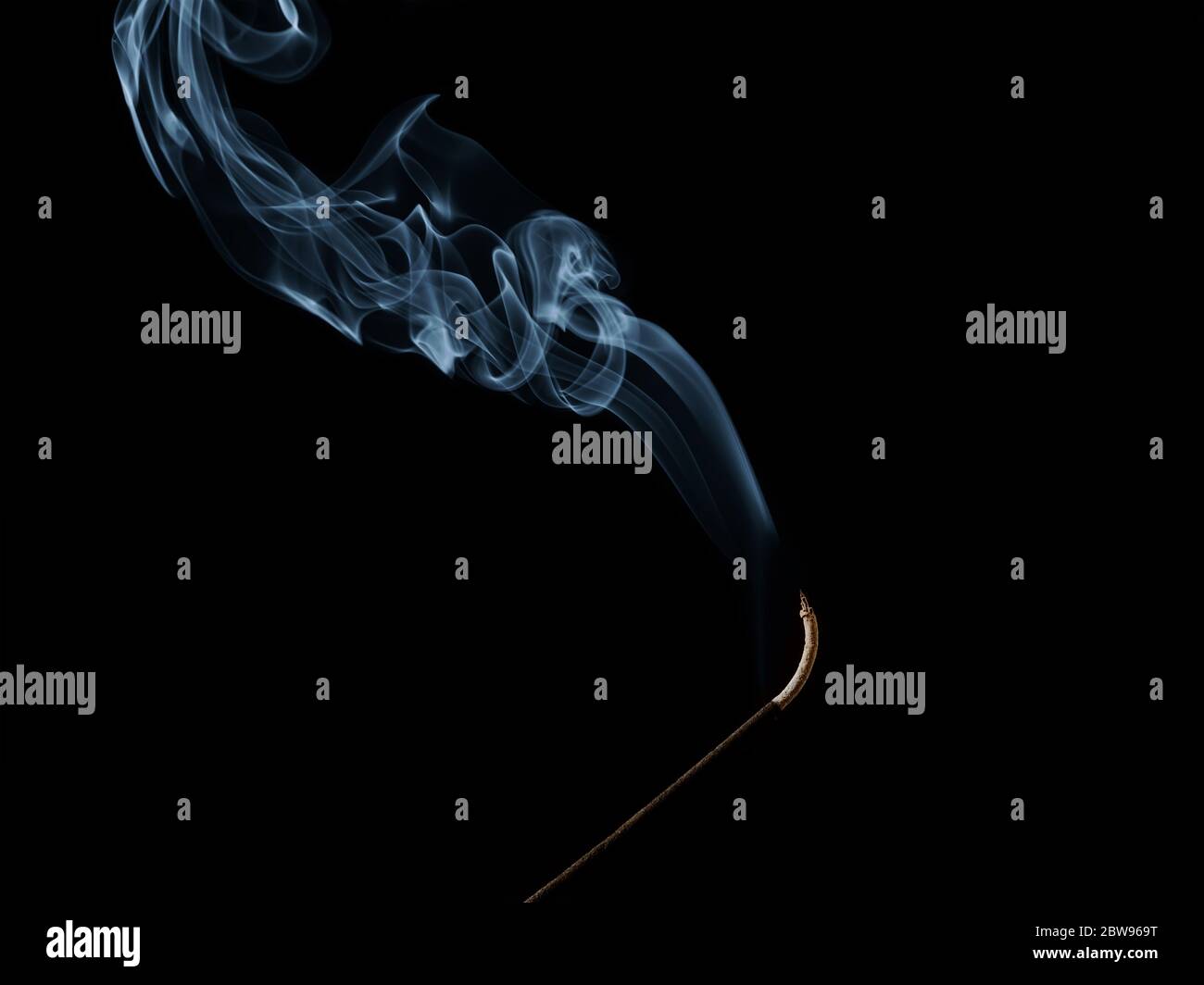 Blue curls of fragrant smoke picturesquely rise above smoldering incense stick on black background. Fragrant Sandalwood for aromatherapy and buddhism Stock Photo