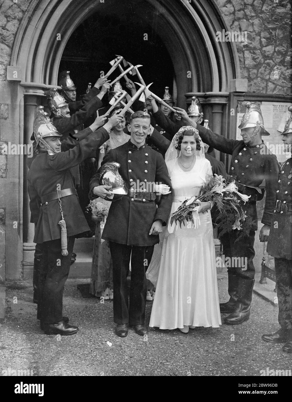 Teddington fire brigade form archway of axes and hoses at wedding of fireman at Teddington . The Teddington Fire Brigade formed an archway of axes and hoses when they acted of honour at the wedding of Fireman F Hathaway , one of their members and Miss A Audus . The bride and groom leaving Christ Church . 13 August 1932 Stock Photo