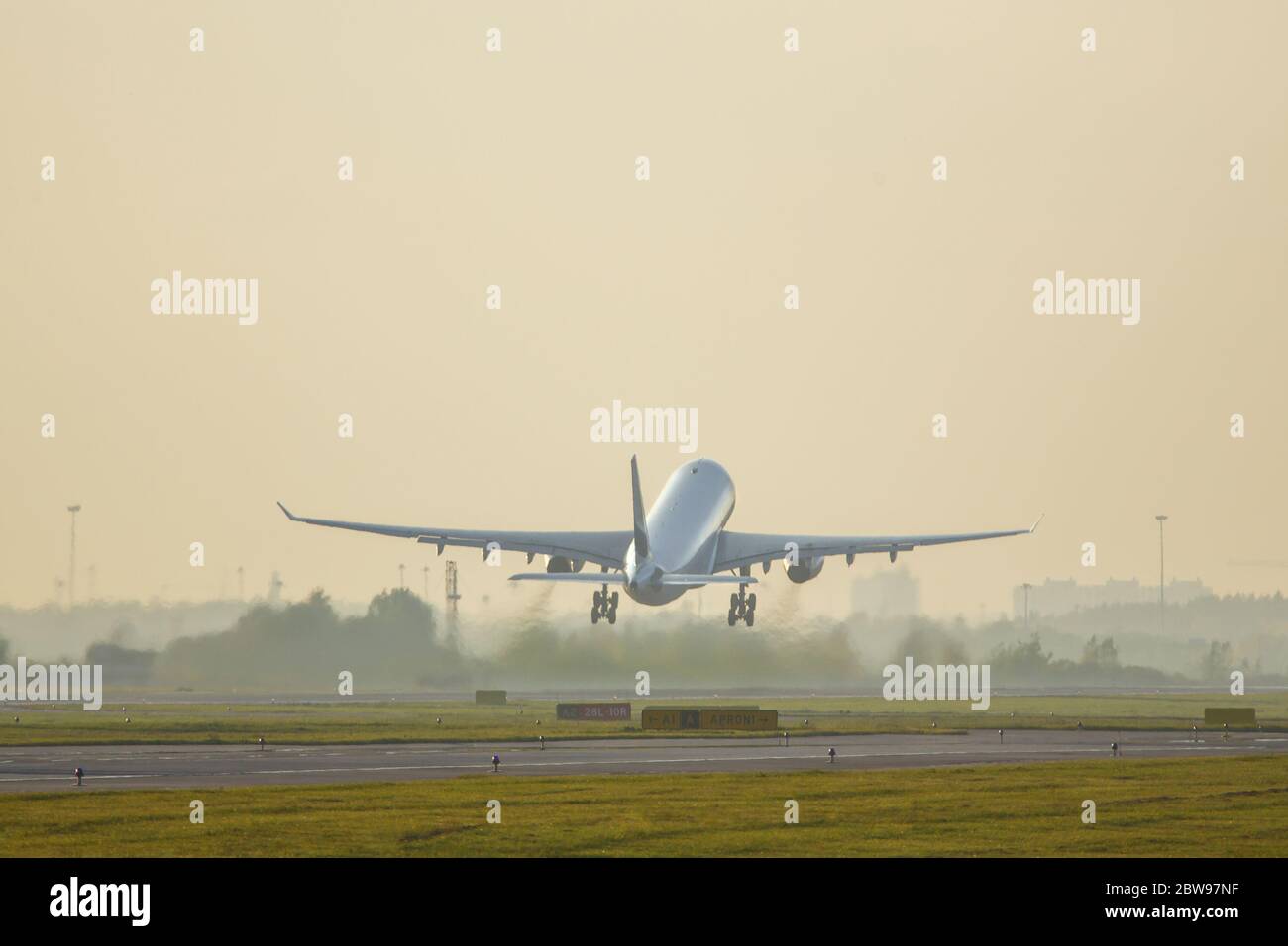 Wide-body passenger airliner taking off on sunset above the runway, back view, copy space. Plane fly up, yellow sky on background, soft focus. Vacatio Stock Photo