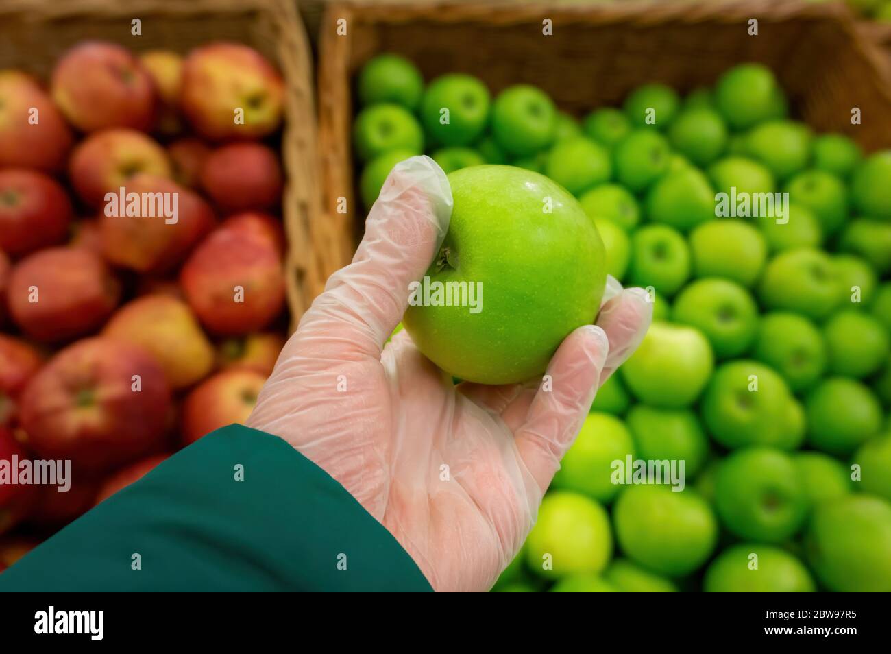 the buyer picks apples in the store and wears protective gloves, maintaining hygienic safety and measures due to the quarantine situation and the risk Stock Photo