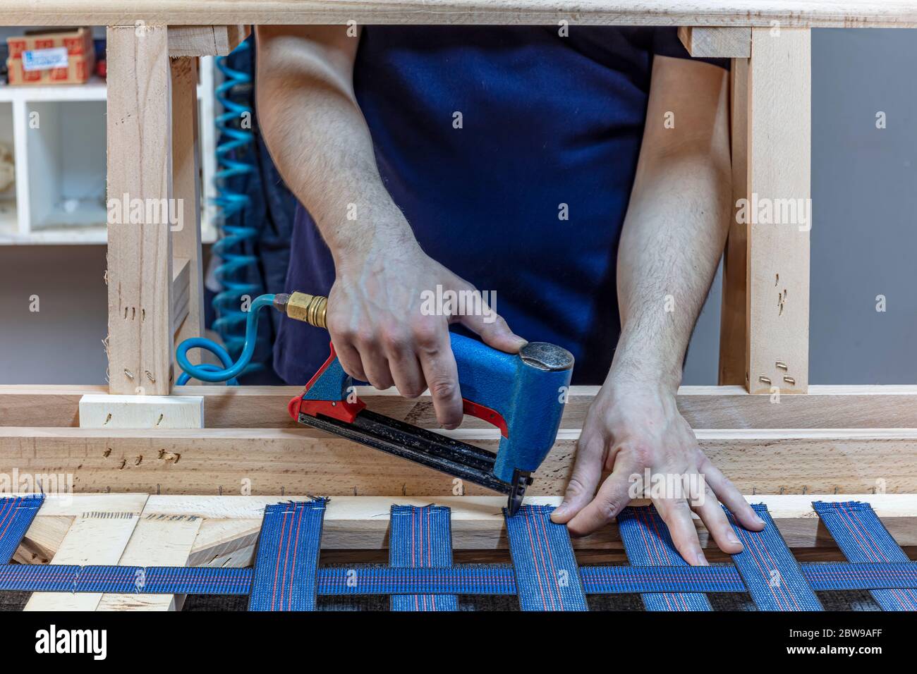 Manufacture of Furniture Seats. Professional male carpenter upholstering vintage armchair in repair shop. Stock Photo