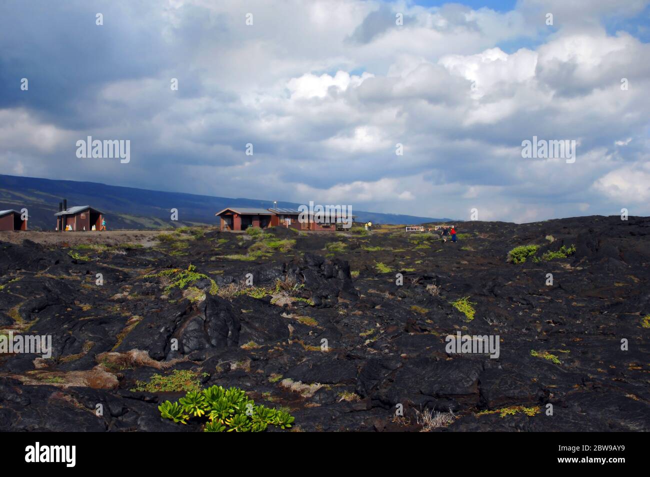 Vog and clouds cover blue sky over the Hawaii Volcanoes National Park.  Crusted lava field and ranger station sit at the end of Chain of Craters Road Stock Photo