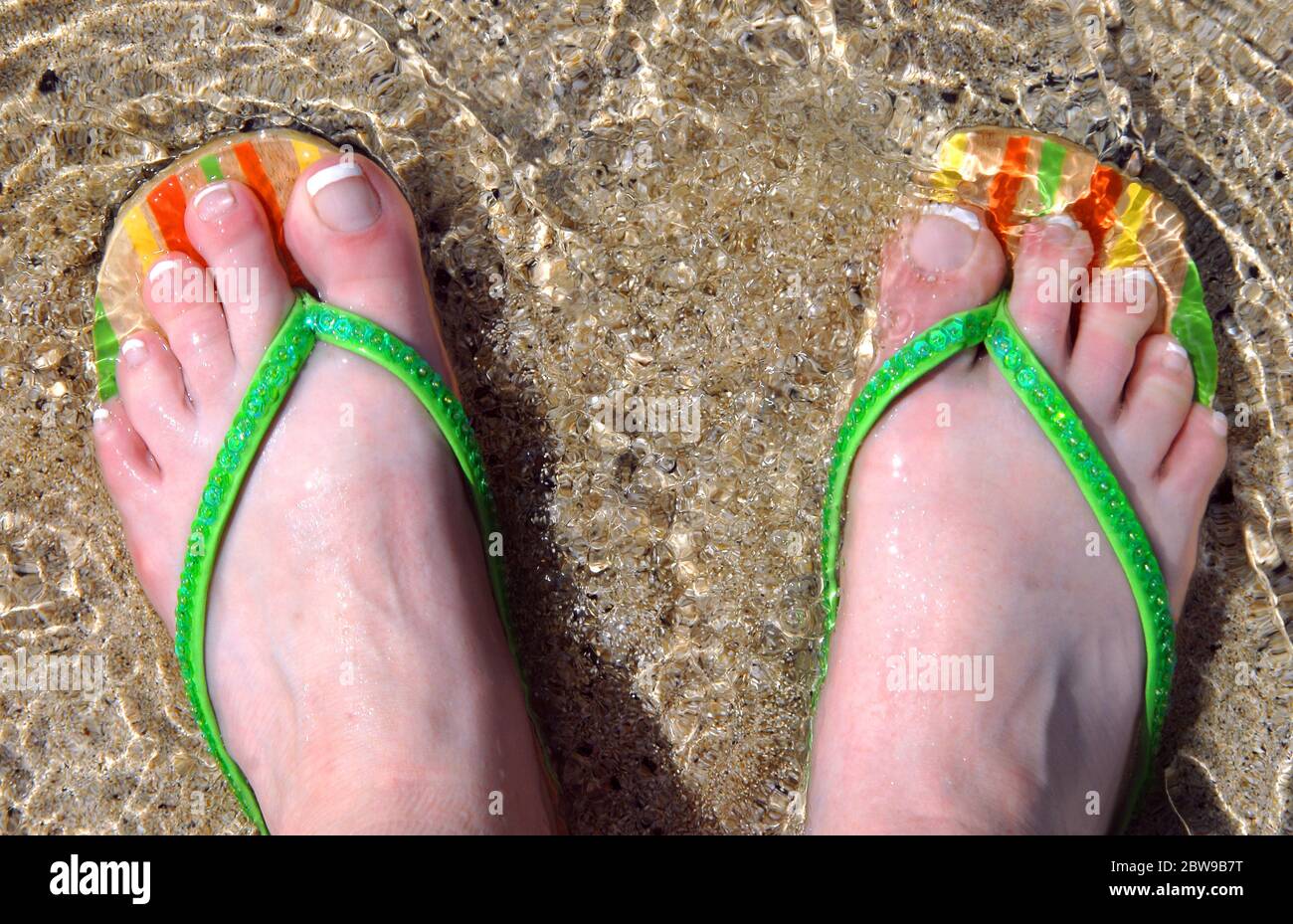 Woman's feet are covered with a gentle wave of water as she explores the  beaches of the Big Island of Hawaii. Flip flops are wooden with orange,  yell Stock Photo - Alamy
