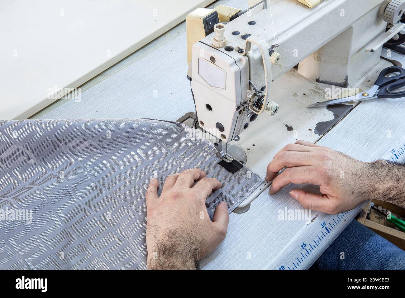 Tailor stitched seat fabrics. Close-up on man working with her sewing machine stitching a long length of fabric. Stock Photo