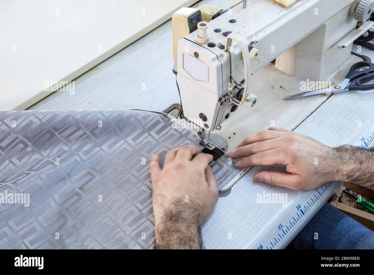 Tailor stitched seat fabrics. Close-up on man working with her sewing machine stitching a long length of fabric. Stock Photo