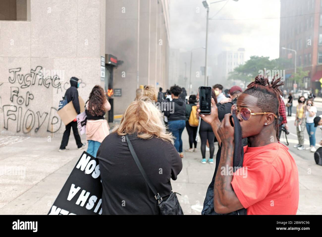 A protester covers their face from smoke and tear gas in downtown Cleveland, Ohio, USA during a major demonstration against police brutality.  Thousands marched to the Justice Center where they had a standoff with police during which tear gas and pepper spray were used on demonstrators throughout the day.  The demonstration is one of many going on in the United States in response to injustice and racism which was sparked by the murder of George Floyd in the hands of police in Minneapolis. Stock Photo