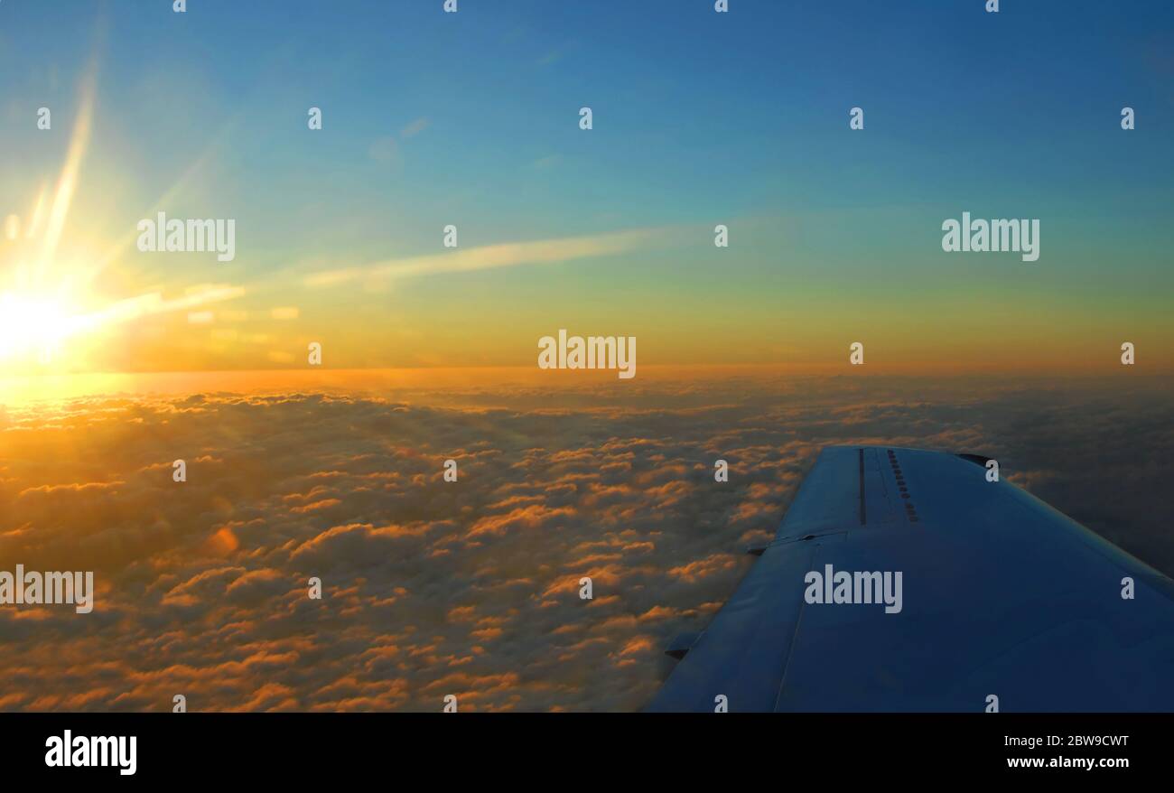 Morning sunlight burns across the clouds painting them orange and golden.  Airplane wing cuts across bottom of image.  Overnight flight to Hawaii gree Stock Photo