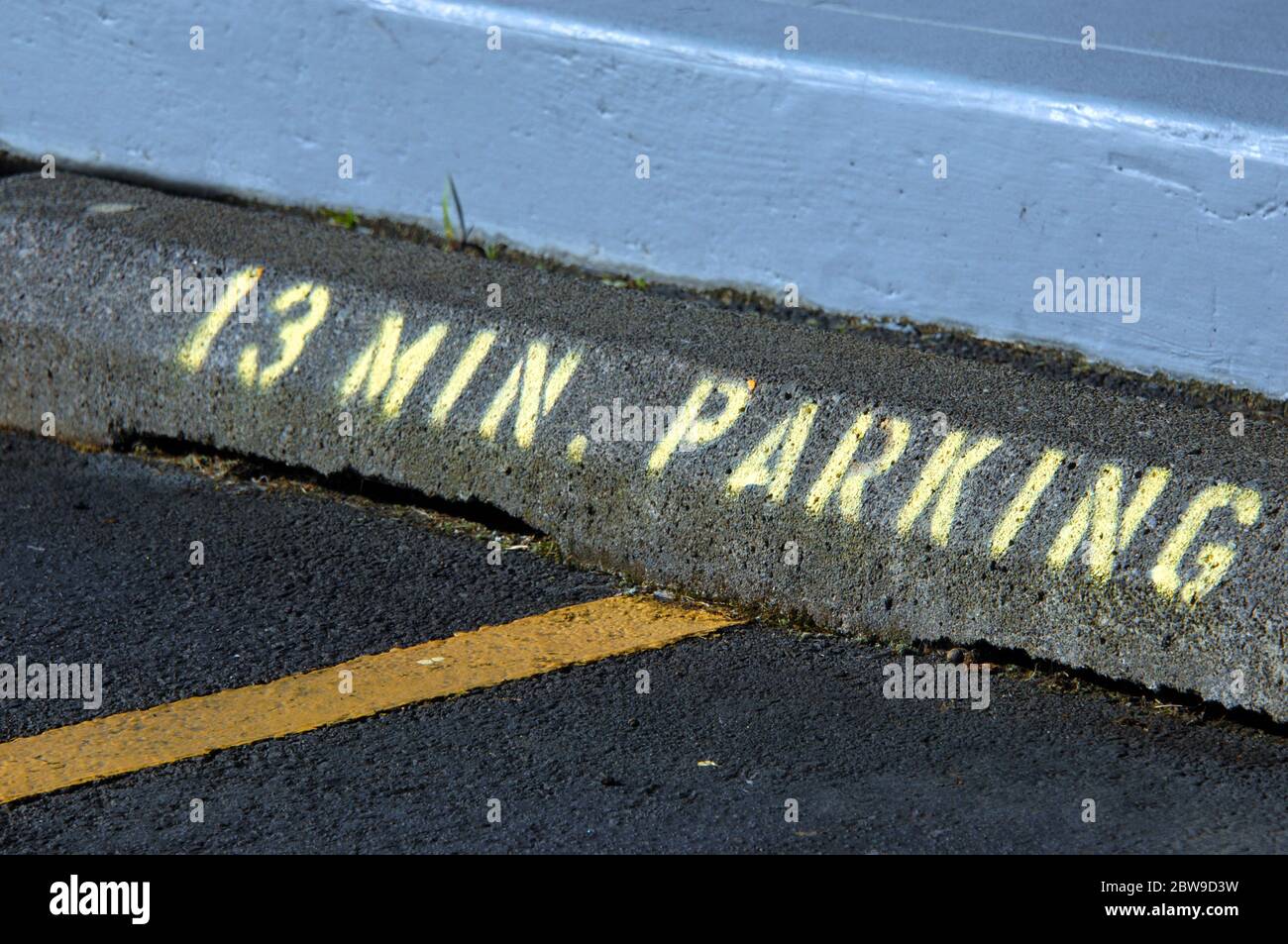 Unusual, and random, time limits parking to 13 minutes.  Concrete curb has stenciled lettering and numbers in yellow spray paint. Stock Photo