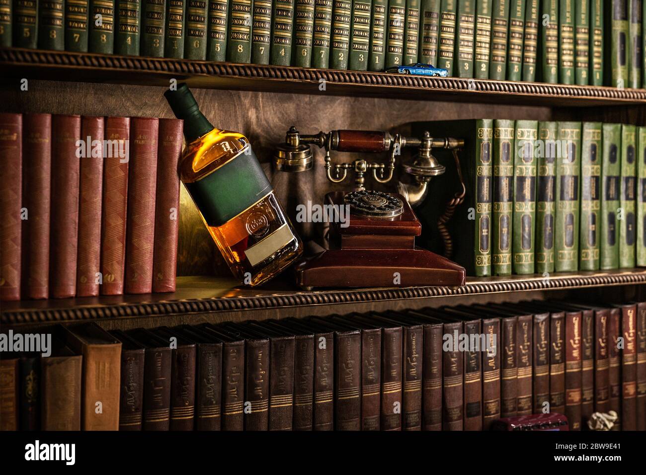Bottle with alcohol on a background of vintage books. Old retro telephone, authentic interior Stock Photo
