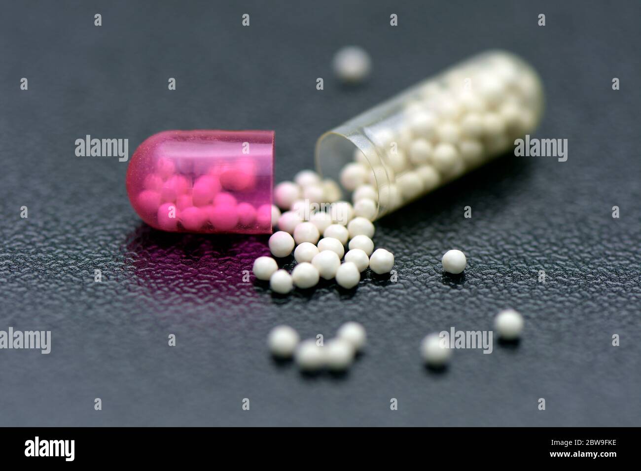 Transparent capsule with sustained release granule. Pellets in transparent hard gelatin capsule on dark background. Stock Photo
