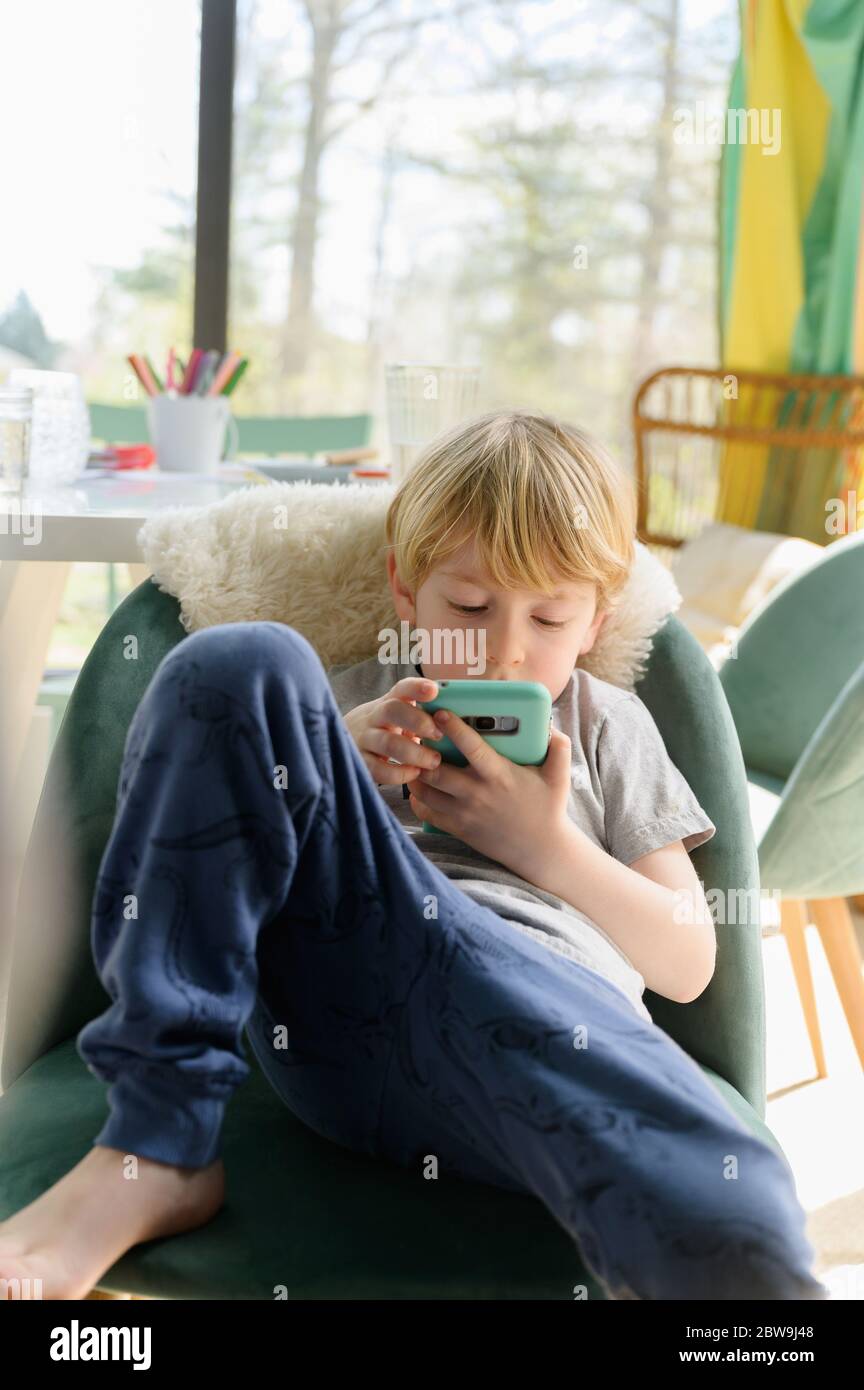 Boy (4-5) sitting in living room with smart phone Stock Photo