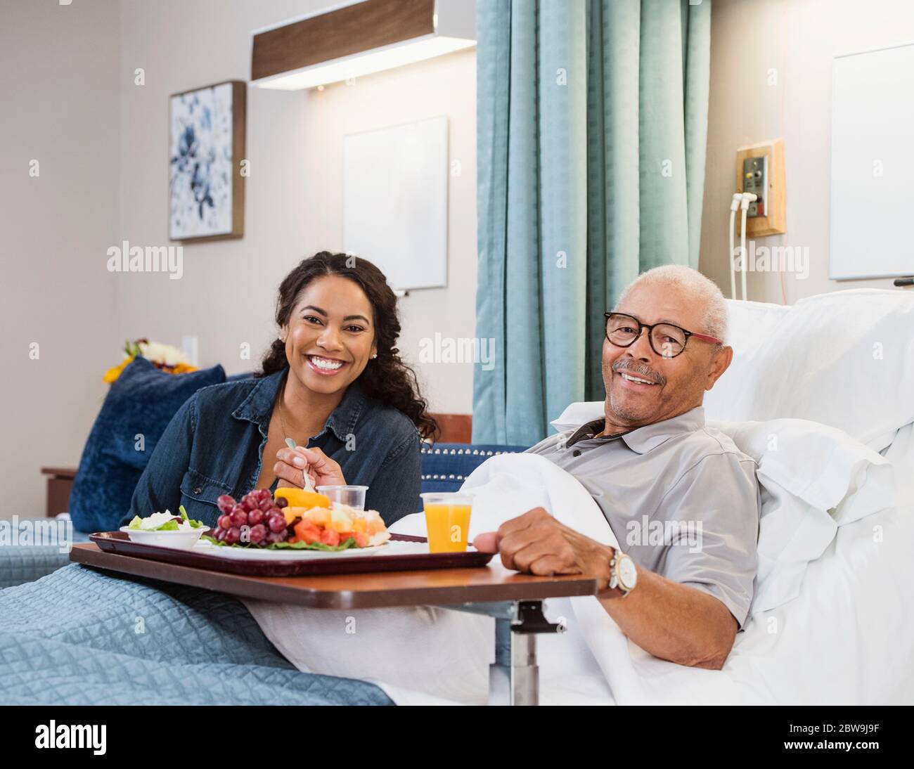 Daughter visiting senior father eating healthy meal in bed in nursing home Stock Photo