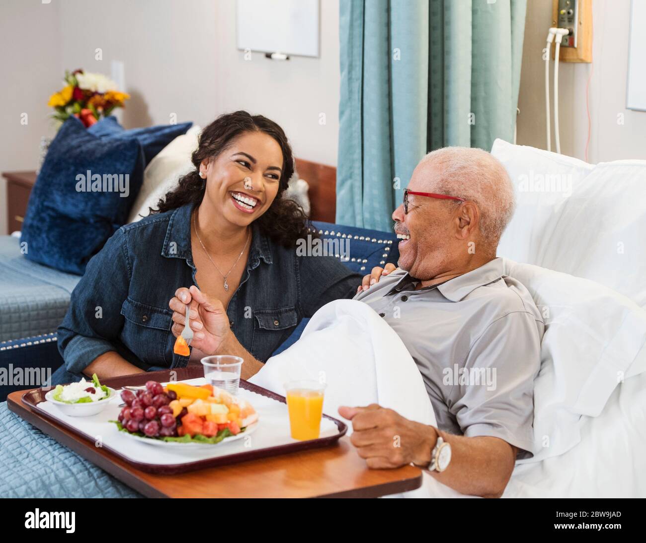 Daughter visiting senior father eating healthy meal in bed in nursing home Stock Photo