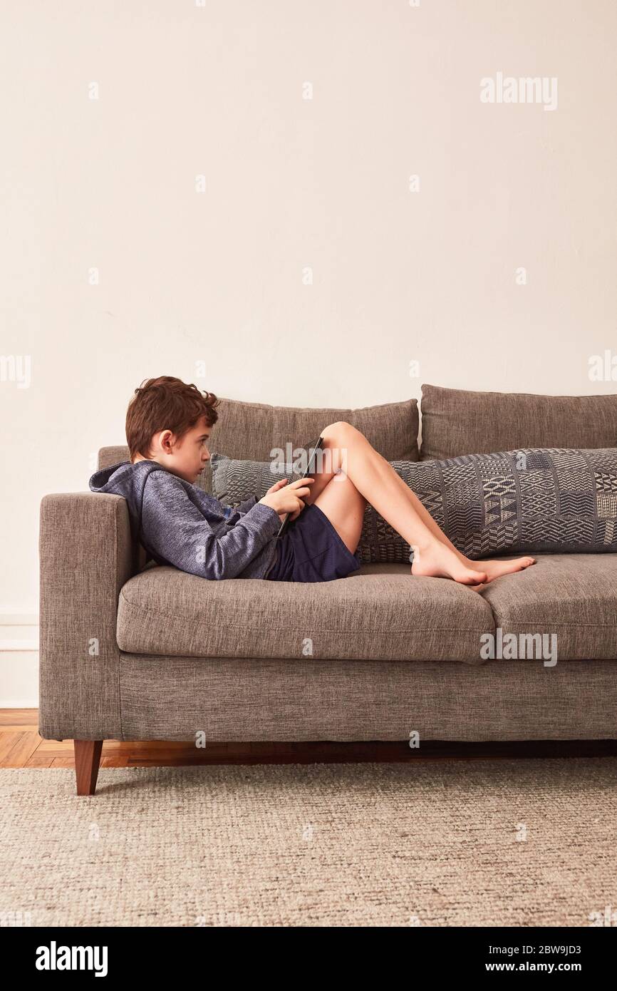 Boy (8-9) using tablet on sofa Stock Photo