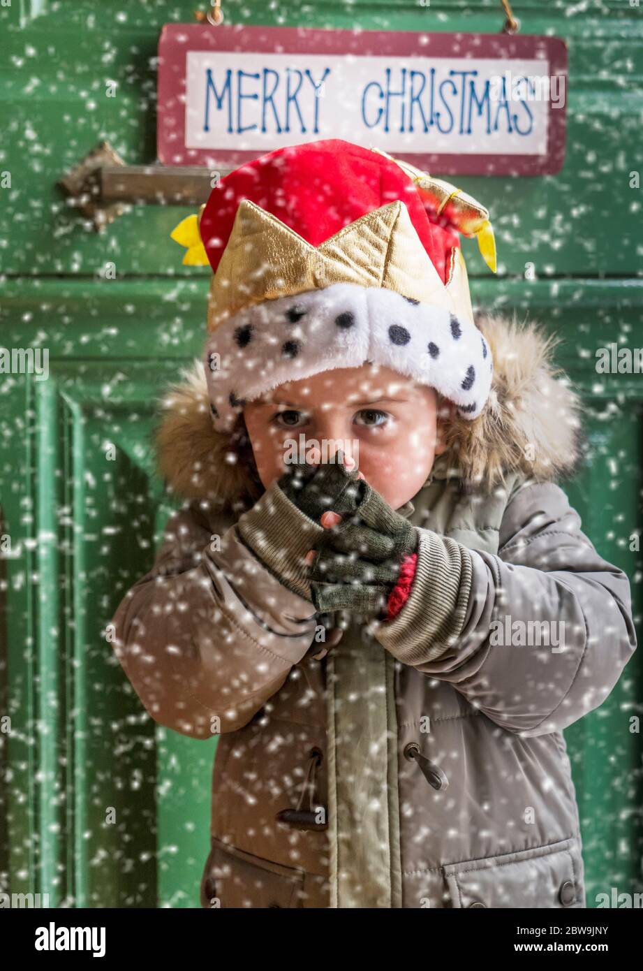 Boy wearing parka and Christmas hat during snowfall in front of green door Stock Photo