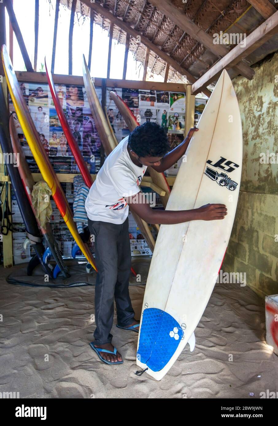 A man sanding a surfboard at the Dizzy Surf Shop where he works. It is