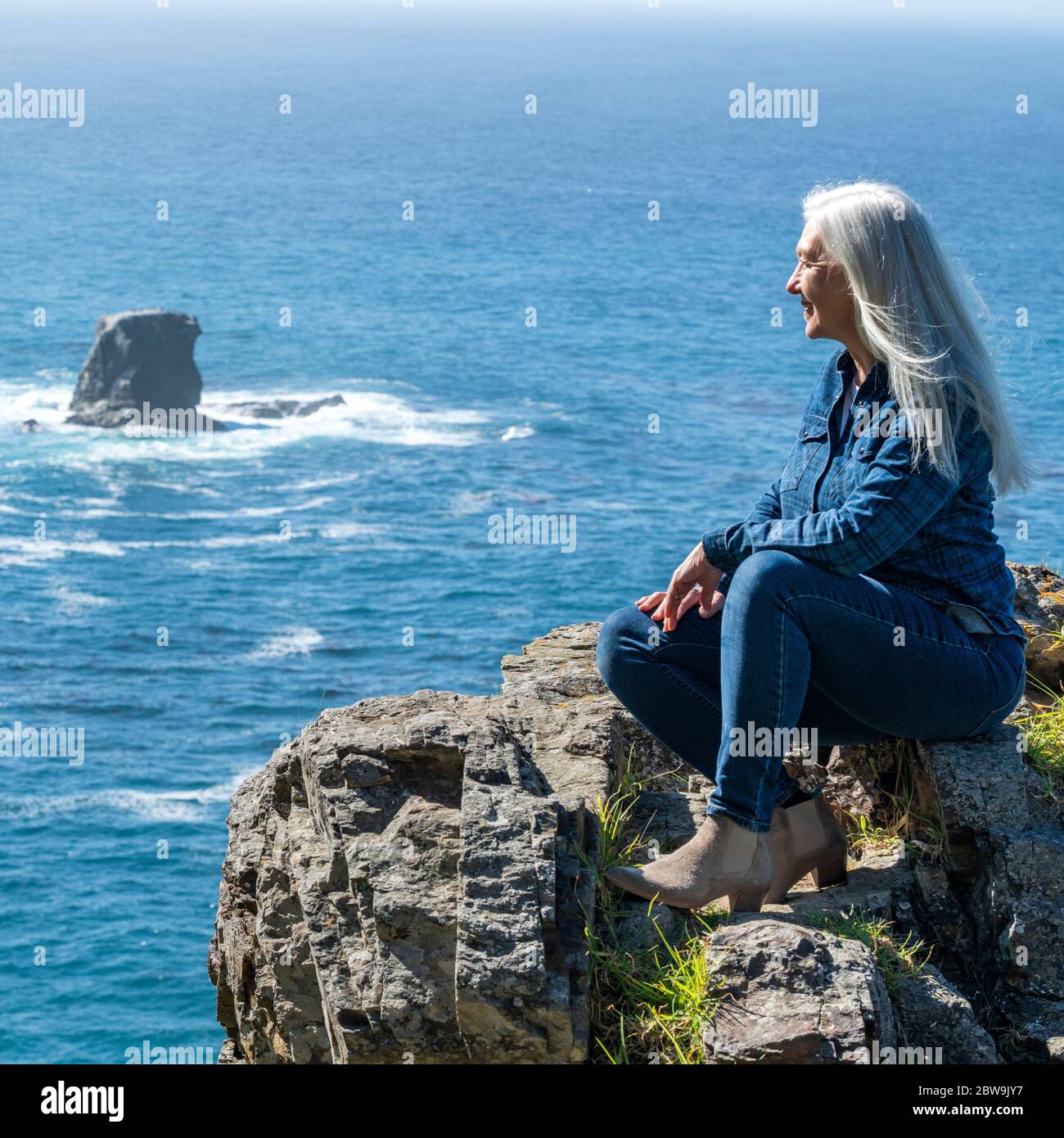 USA, California, Big Sur, Woman sitting at the edge of cliff looking at view Stock Photo