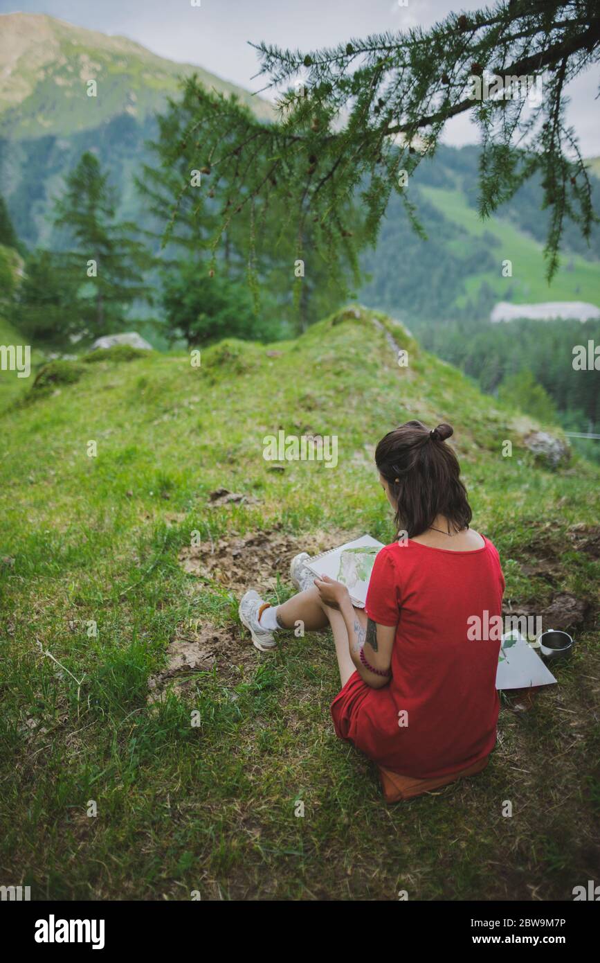 Switzerland, Obergoms, Young woman painting with watercolor in Swiss Alps Stock Photo