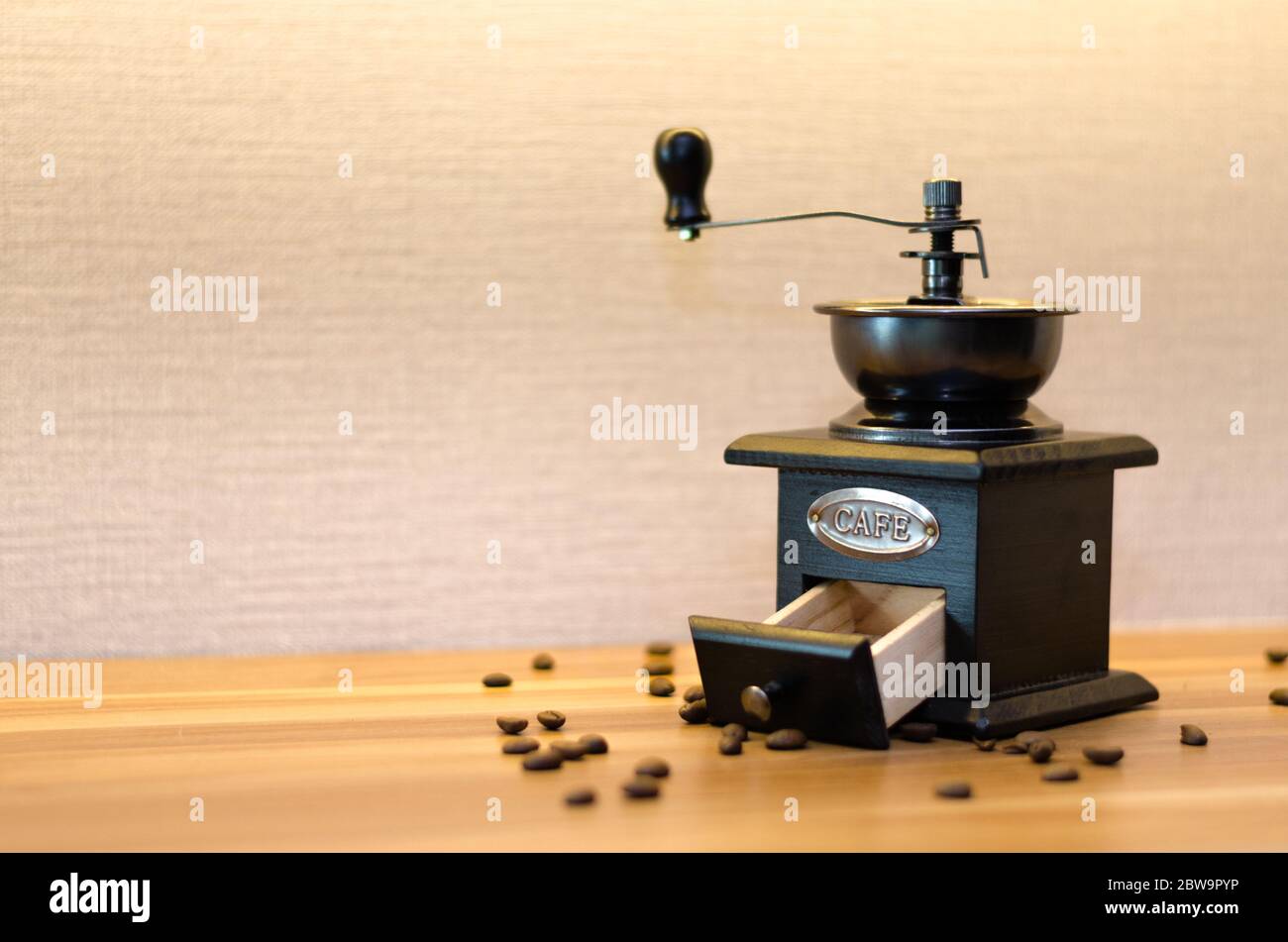 A coffee grinder with an open drawer and messy coffee beans on a wood