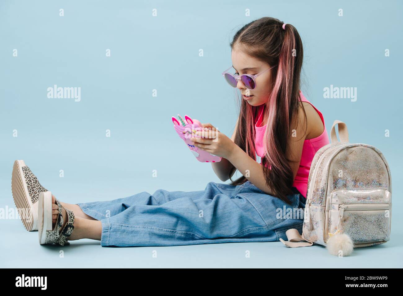 Happy little girl in a pink shirt sitting on the floor, browsing in her phone Stock Photo