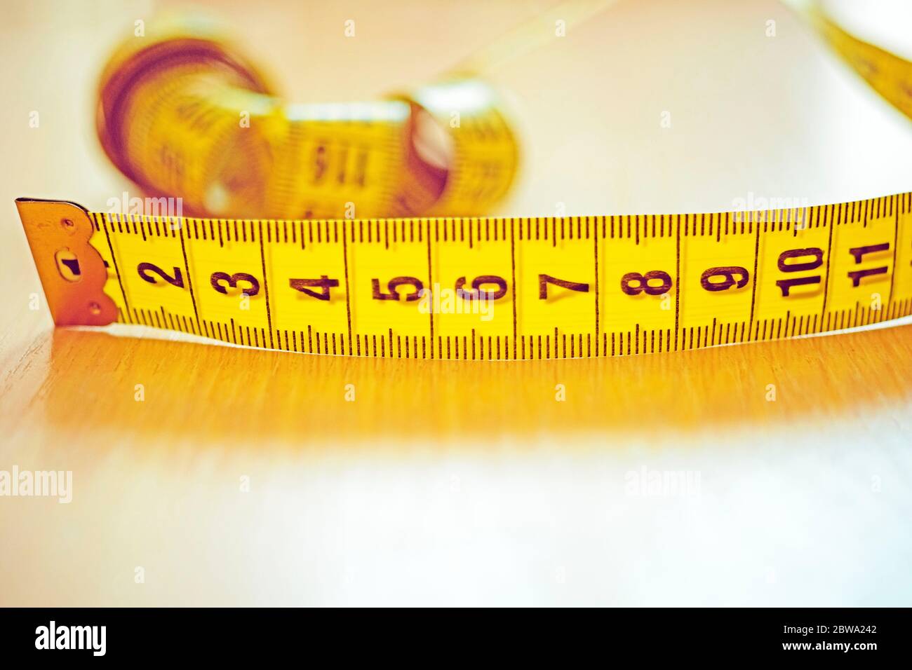 Yellow measuring tape with black scale on the wooden table. Stock Photo