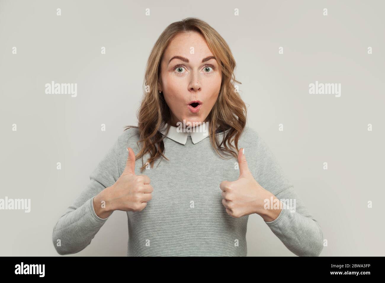 Surprised woman showing thumb up on white Stock Photo - Alamy