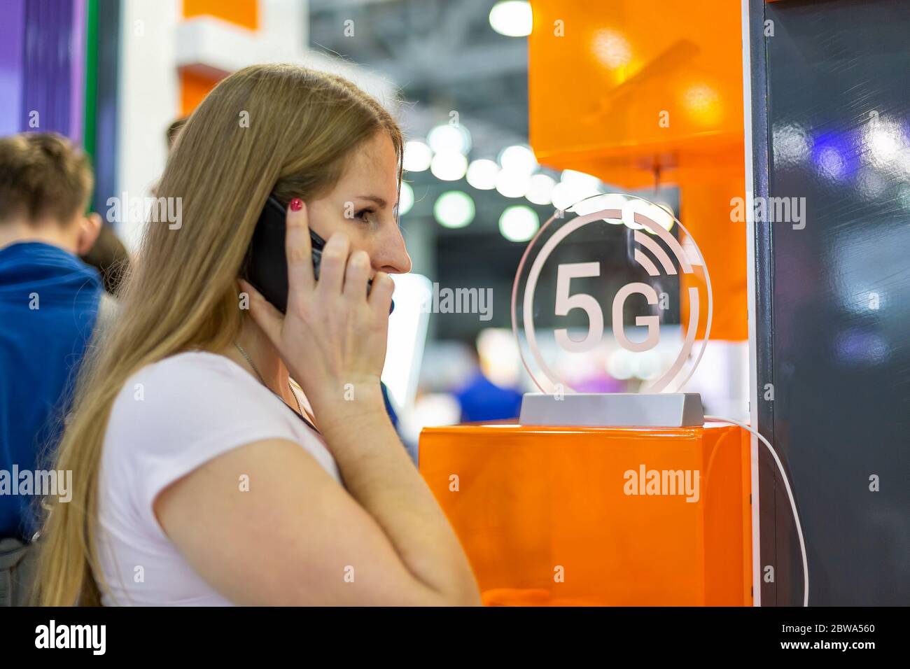 young caucasian girl talking on a smartphone on the background of the 5g icon. background blur, soft focus Stock Photo