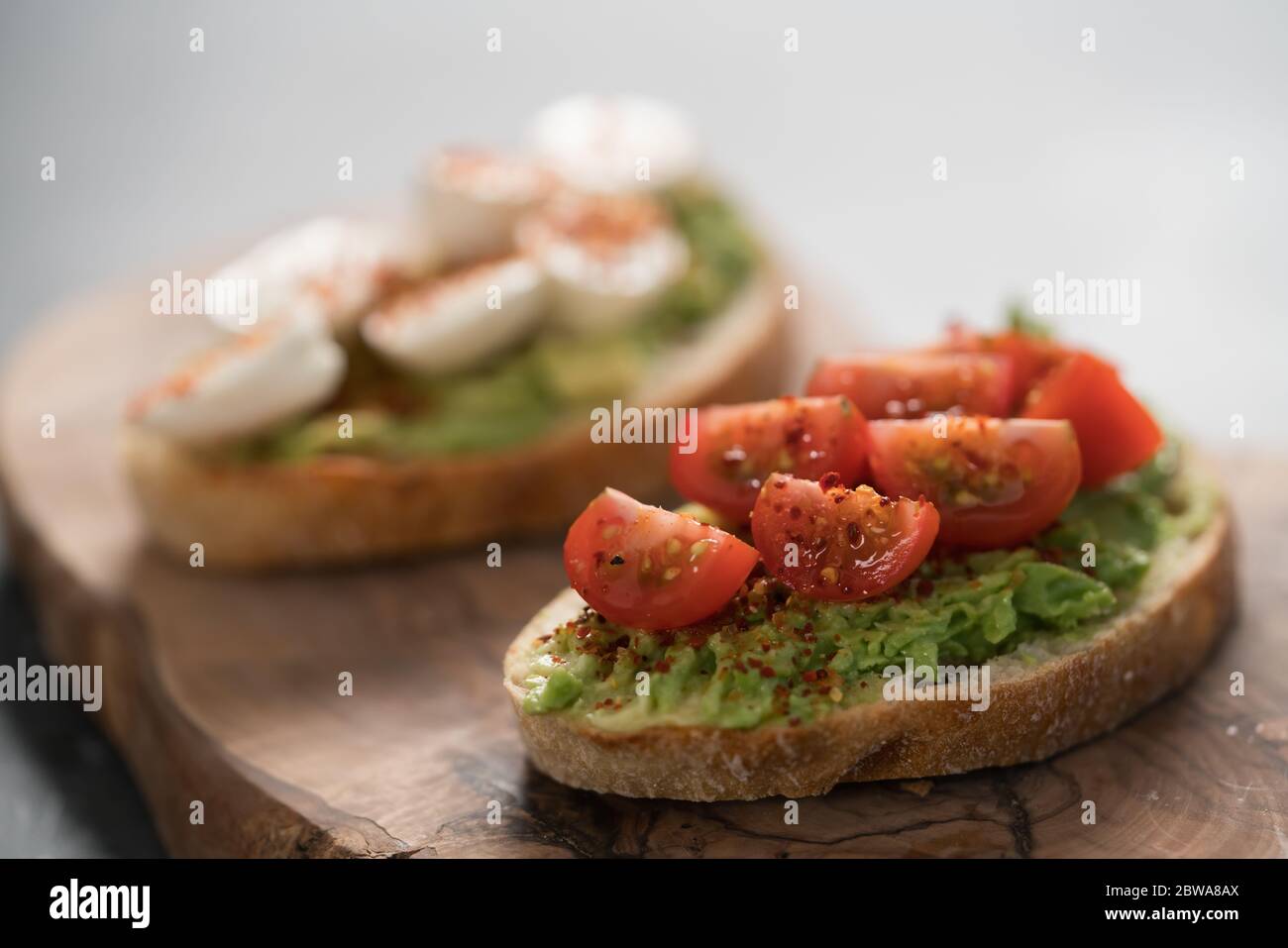 Bruschettas with avocado, tomato and mozzarella on wood board on concrete bacground Stock Photo